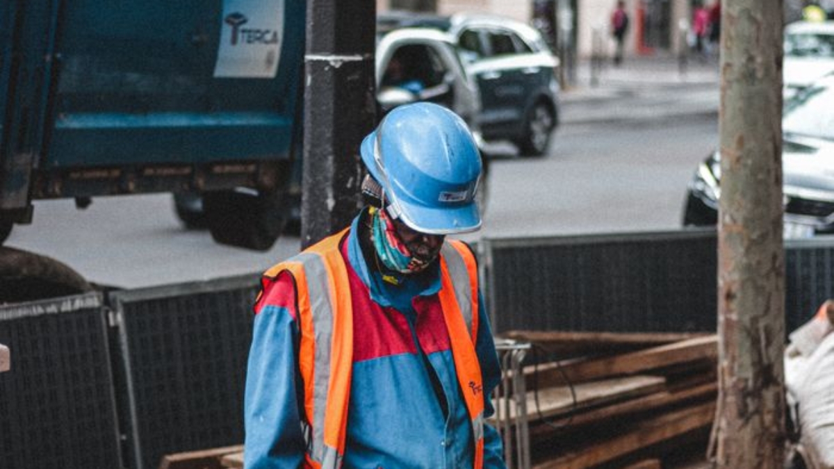 Side view of male worker in protective helmet and uniform standing on construction site in big contemporary megapolis